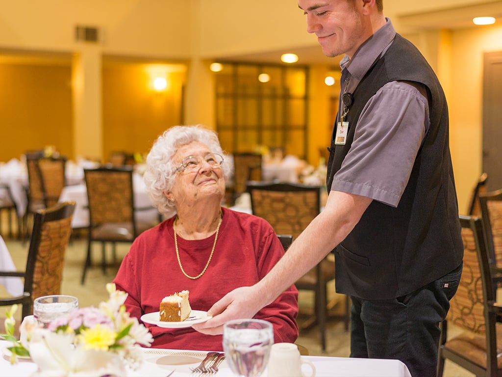 senior resident being served cheesecake at one of our dining venues
